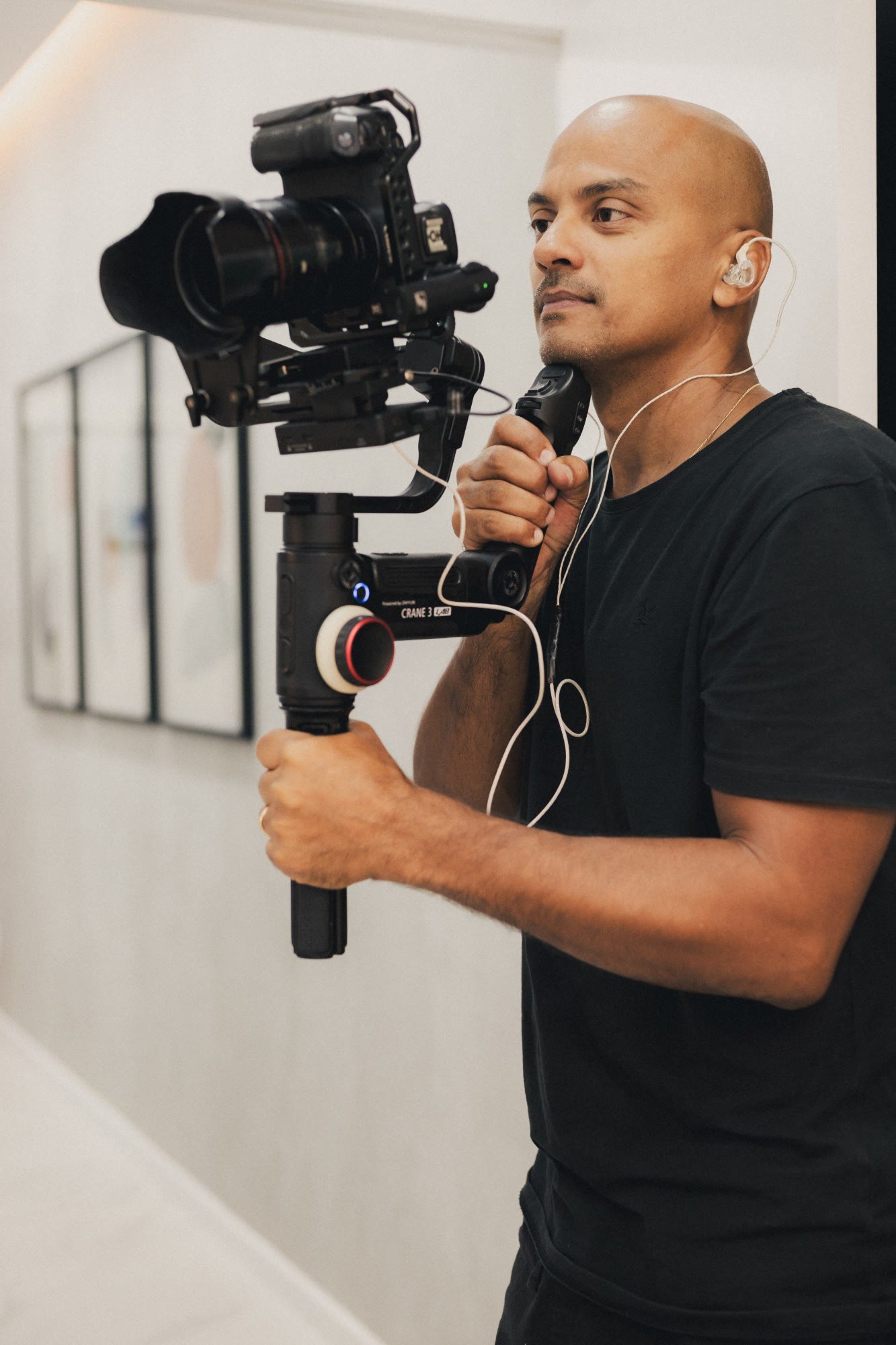 Paulo H Lima, fotógrafo e videomaker de moda, com uma câmera montada em estabilizador, de camiseta preta e fone de ouvido